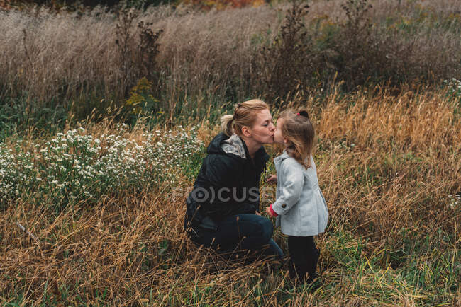 Mid adult woman kissing toddler daughter in field of long grass — Stock Photo