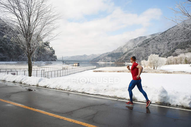 Corredor masculino corriendo a lo largo de la carretera en invierno, Lago Kawaguchiko, Monte Fuji, Japón - foto de stock