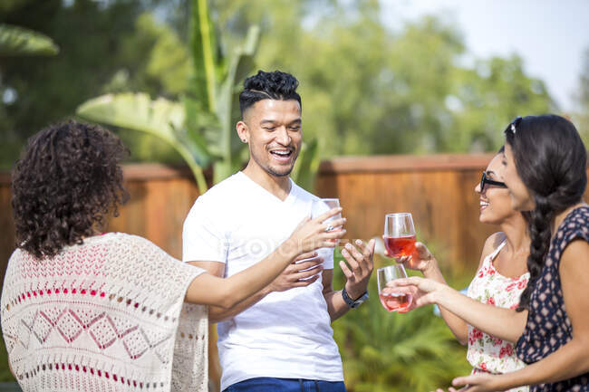 Молодий чоловік ділиться тостами трояндового вина з дорослими сестрами в саду — стокове фото