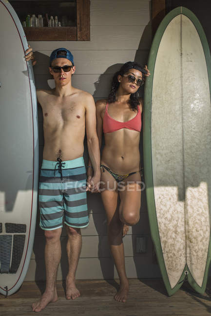 Portrait of cool young surfing couple standing on porch, Rockaway Beach, New York State, USA — Stock Photo