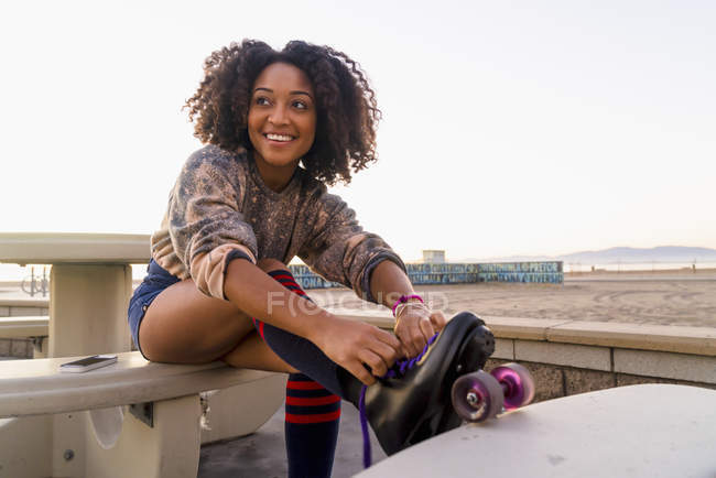Femme adulte moyenne assise à l'extérieur, attachant des patins à roulettes — Photo de stock