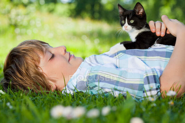 Niño en el prado abrazando a un gato - foto de stock