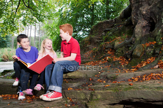 Tres niños disfrutando de un libro juntos - foto de stock