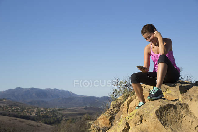 Femme coureuse choisissant la musique smartphone au sommet de la colline, Thousand Oaks, Californie, États-Unis — Photo de stock