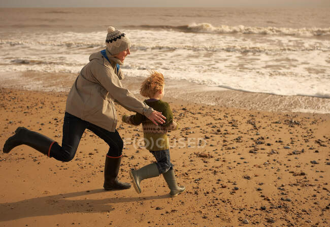 Mulher correndo brincando com menino na praia — Fotografia de Stock