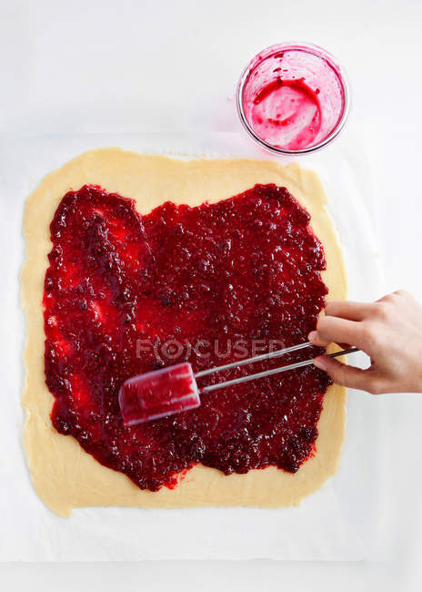Hand spreading jam on dough — Stock Photo