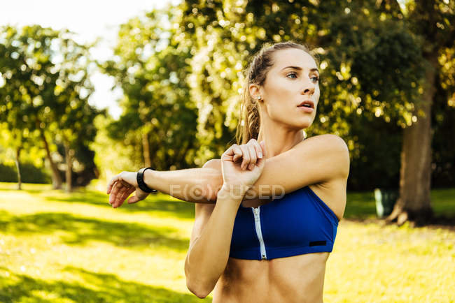 Mujer joven entrenando, estirando brazos cruzados en el parque - foto de stock