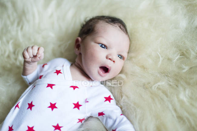 Новорожденный мальчик лежит на пушистом одеяле и смотрит в сторону. — стоковое фото