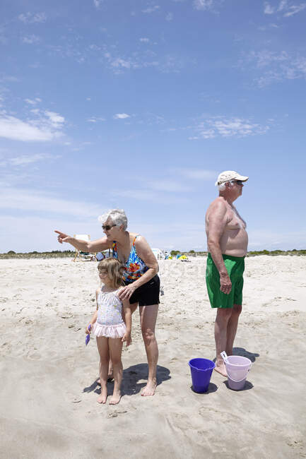 Senior woman with granddaughter pointing and looking out on beach — Stock Photo