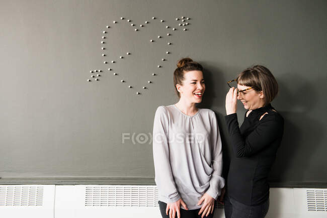 Dos mujeres por pared con forma de corazón - foto de stock