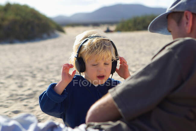 Garçon écoute écouteurs sur la plage — Photo de stock