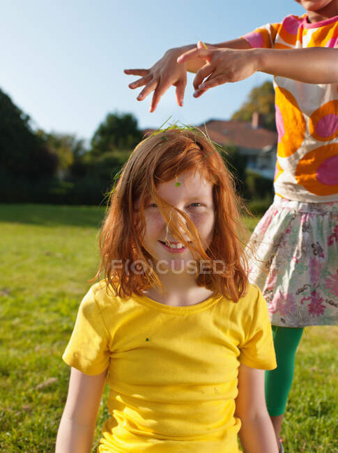 Girl putting grass on friends head, portrait — Stock Photo