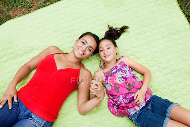 Мать и дочь лежат на одеяле, держась за руки — стоковое фото