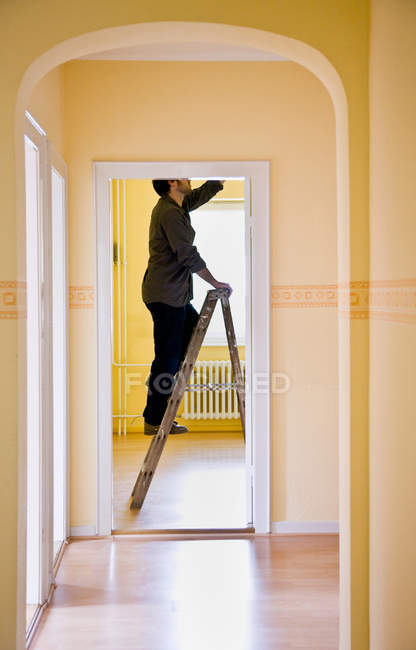 Mann wechselt Glühbirne auf Leiter — Stockfoto