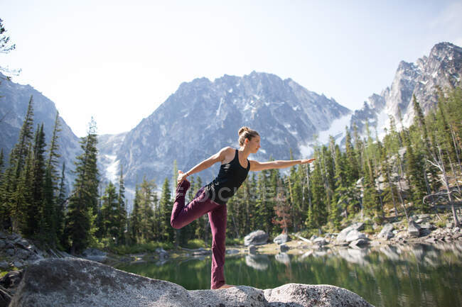 Young woman standing on rock beside lake, in yoga pose, The Enchantments, Alpine Lakes Wilderness, Washington, USA — Stock Photo