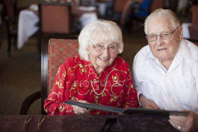 Portrait of senior couple sitting at table in restaurant, smiling — Stock Photo