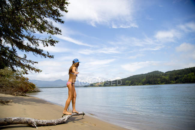 Junge Frau im Bikini balanciert auf einem Ast am Strand, Nehalem Bay, Oregon, USA — Stockfoto