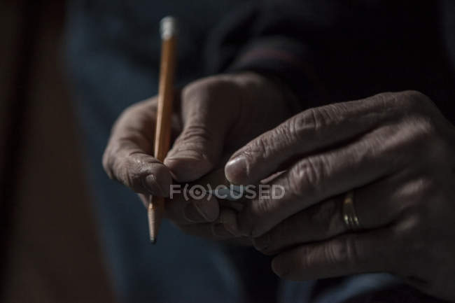 Primo piano di mani maschili che tengono una matita e un pezzo di legno — Foto stock