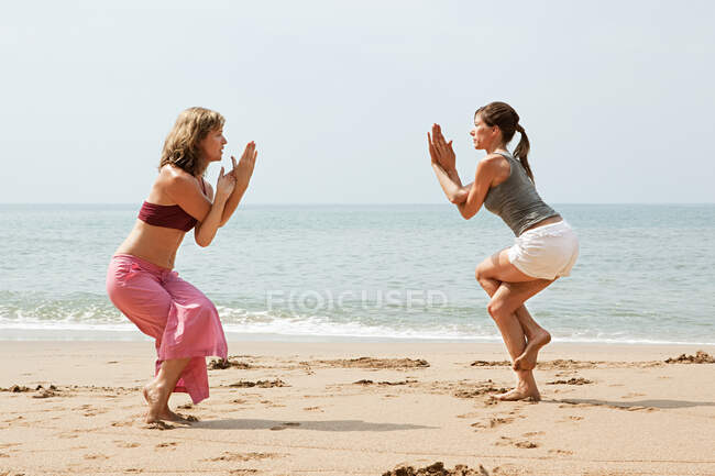 Two women practicing yoga on a beach — Stock Photo