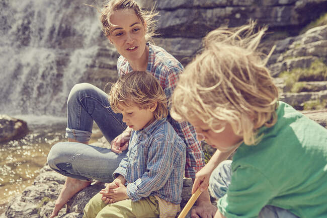 Mother and sons, sitting on rocks by waterfall — Stock Photo