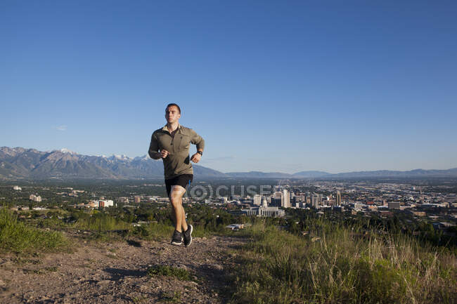 Joven corredor masculino corriendo por la pista por encima de la ciudad en el valle - foto de stock