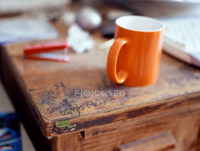Graffiti et tasse orange sur bureau en bois — Photo de stock