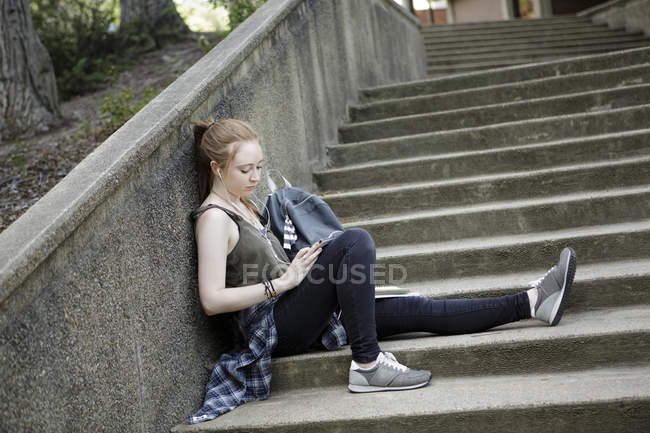 Молода жінка сидить на самоті на сходах слухаючи музику на навушниках — стокове фото