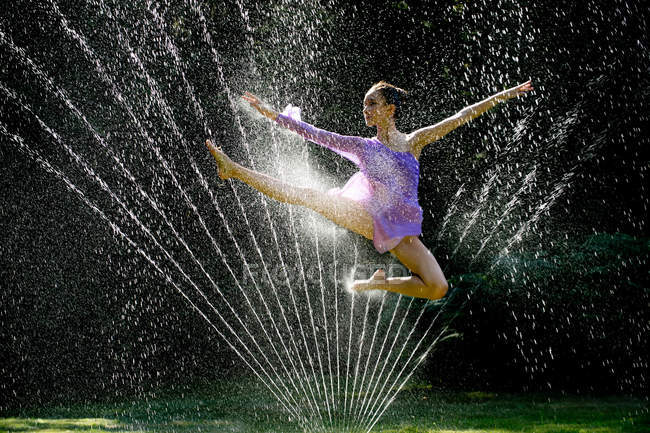 Ballerina jumping over water sprinkler — Stock Photo