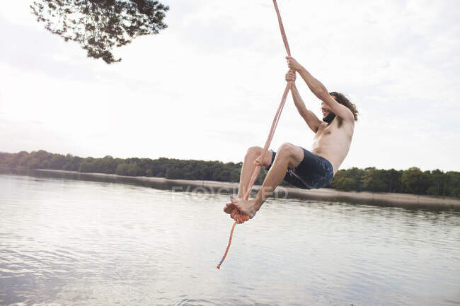 Young man rope swinging above lake — Stock Photo