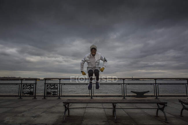 Contemporary african american man exercising by walkway along river using technology — Stock Photo