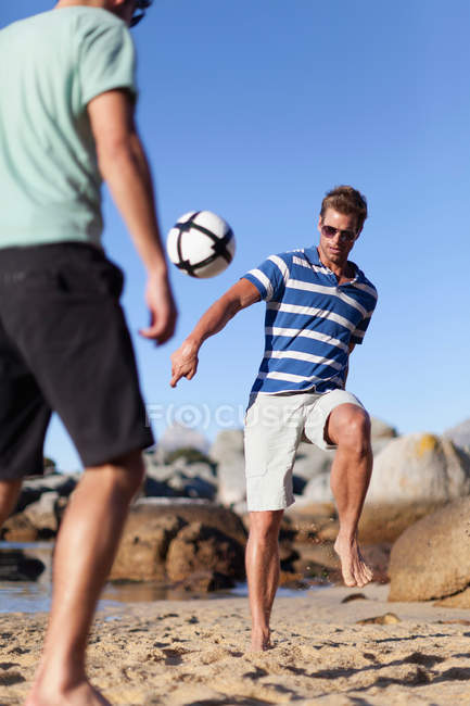 Мужчины играют в футбол на пляже, избирательный фокус — стоковое фото