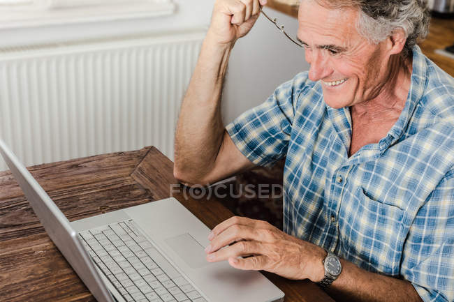 Hombre mayor usando portátil en la cocina - foto de stock
