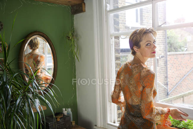 Retrato de una mujer adulta mirando por encima de su hombro mientras abre la ventana - foto de stock