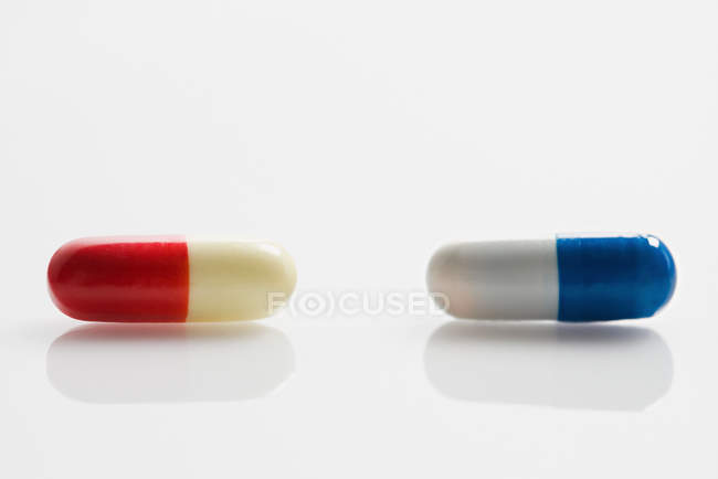 Duas cápsulas vermelhas e azuis sobre fundo branco — Fotografia de Stock