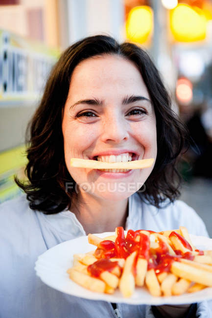Frau hält Pommes in den Zähnen und lächelt — Stockfoto