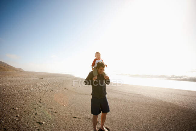 Father carrying son on shoulders along beach — Stock Photo