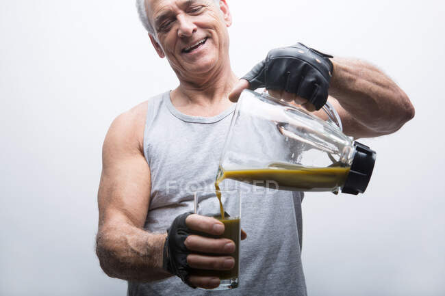 Uomo anziano versando frullato dal frullatore nel vetro — Foto stock