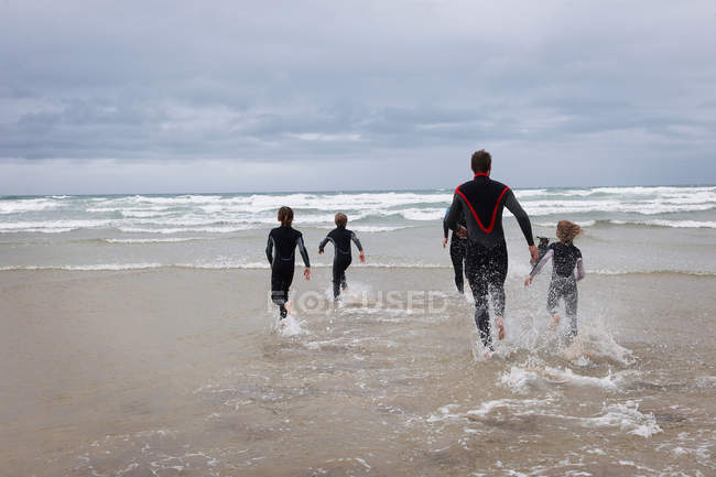 Familia corriendo hacia el mar en trajes de neopreno - foto de stock