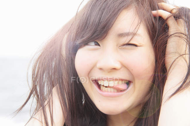 Portrait of young woman, hands in hair, sticking tongue out — Stock Photo