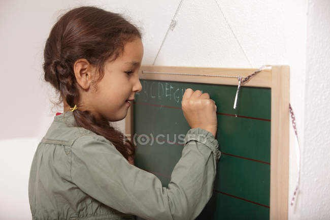 Mädchen schreibt auf kleine Tafel — Stockfoto