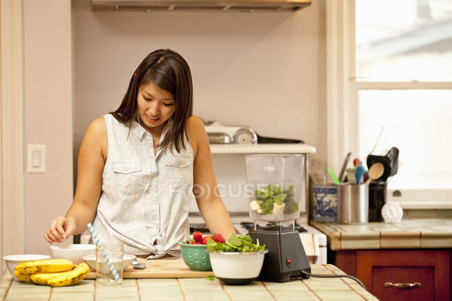 Mujer joven haciendo batido verde en la cocina - foto de stock