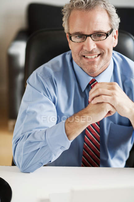 Hombre de negocios sonriente sentado en el escritorio - foto de stock