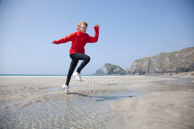 Boy jumping over pools on beach — Stock Photo