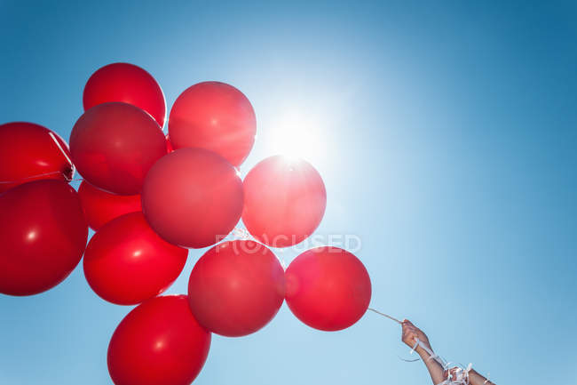 Hands holding bunch of red balloons against blue sky — Stock Photo