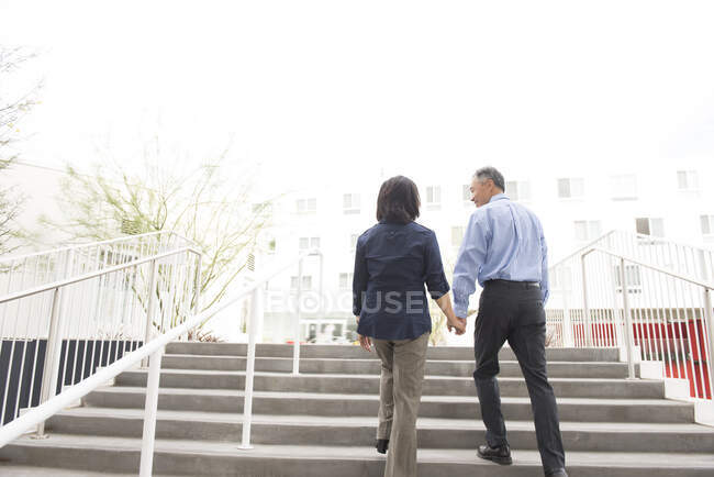 Низкий угол полный вид сзади зрелой пары, держащей за руки поднимающуюся лестницу — стоковое фото
