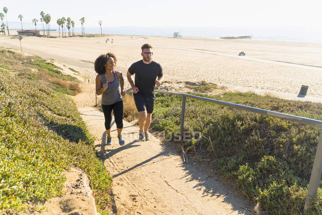 Casal correndo ao longo do caminho pela praia — Fotografia de Stock