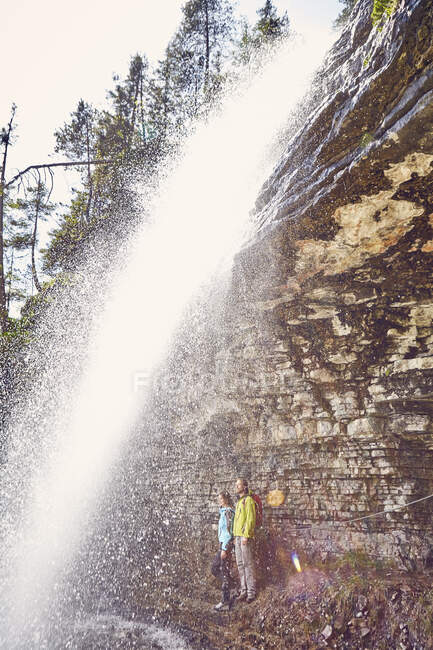 Pareja joven parada debajo de la cascada, mirando hacia fuera, Tirol, Austria - foto de stock