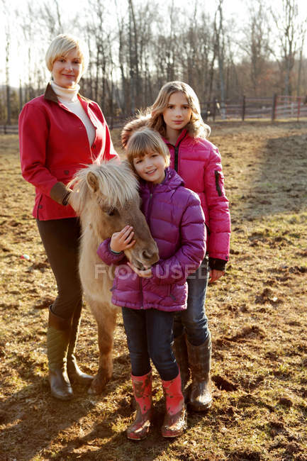 Портрет матери и дочери, стоящие с пони — стоковое фото