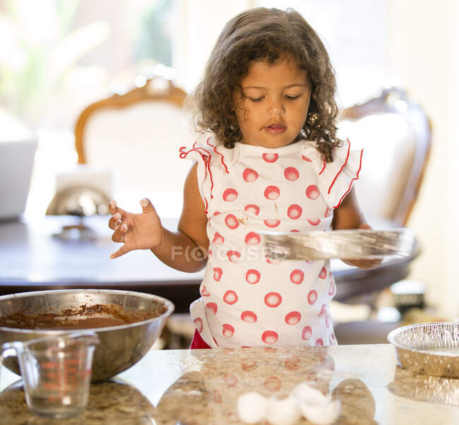Mädchen am Küchentisch hält Kuchenblech und blickt nach unten — Stockfoto
