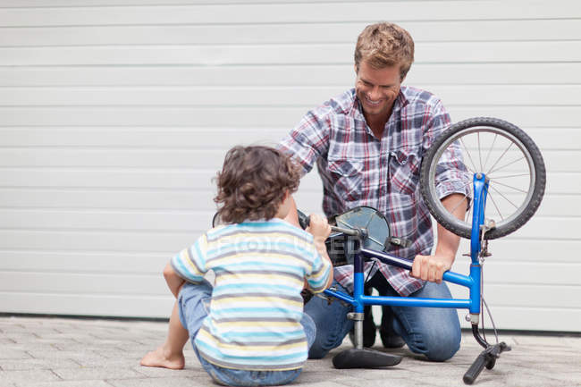Отец помогает сыну чинить велосипед. — стоковое фото